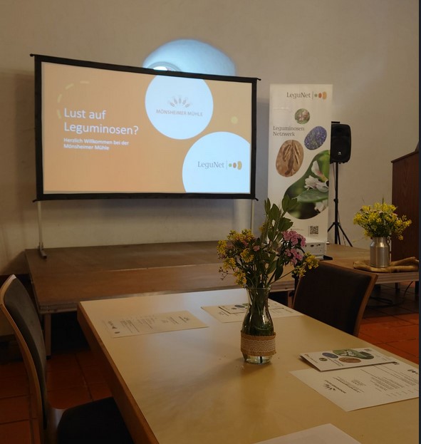 Ein Raum mit einer Leinwand auf der ein Titel für eine Veranstaltung abgebildet ist.